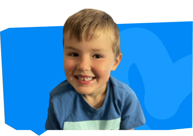 A smiling young boy with short blond hair wears a blue shirt against a blue background.