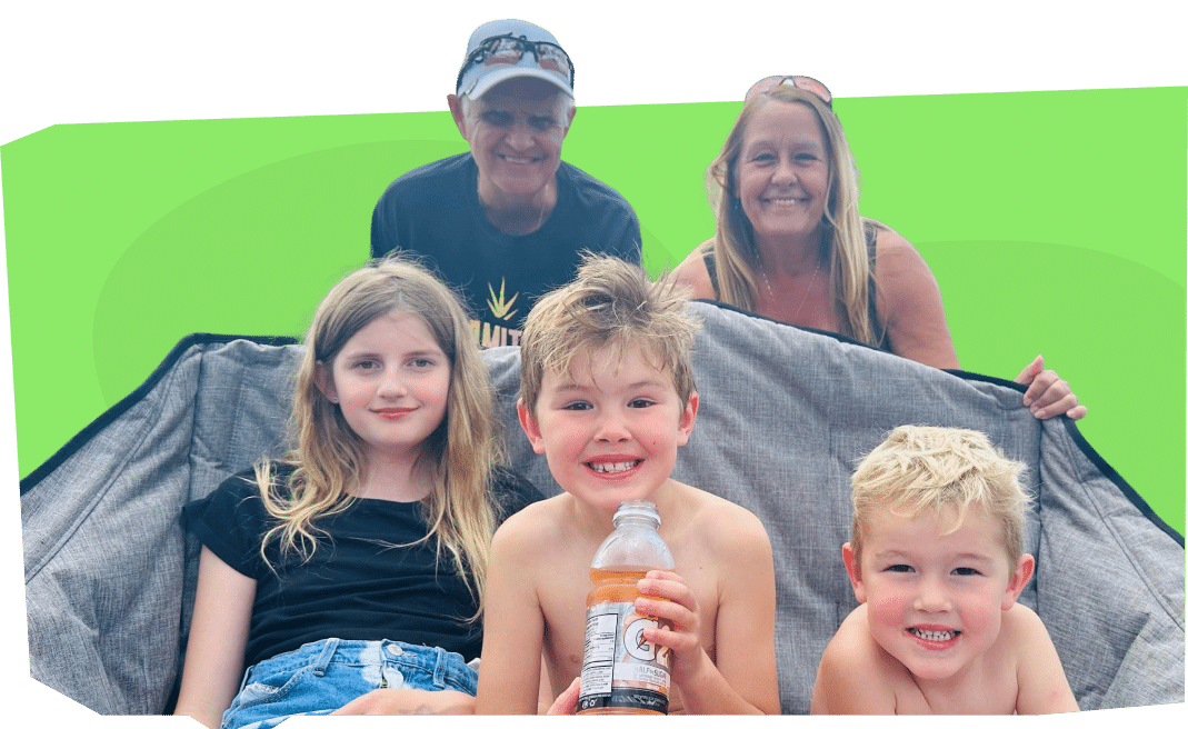 A group of five people, including three children and two adults, are sitting together on a large blanket or mat.
