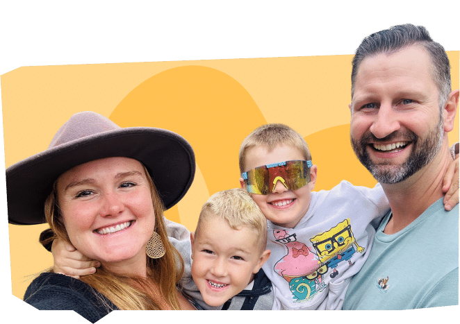 A family photo featuring four smiling members: a woman wearing a hat, a man with a beard, and two young boys, one wearing colorful sunglasses and a cartoon shirt. The background is a simple orange design.