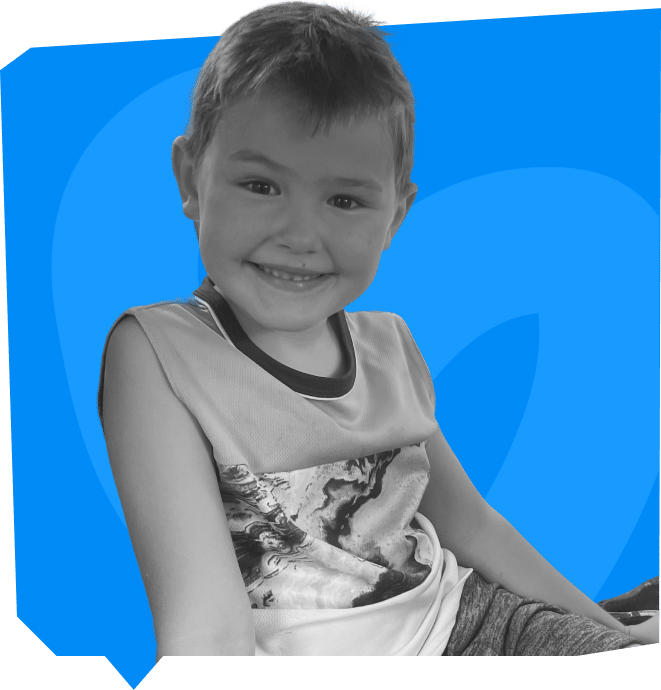 A smiling young boy wearing a sleeveless shirt is sitting against a blue background.