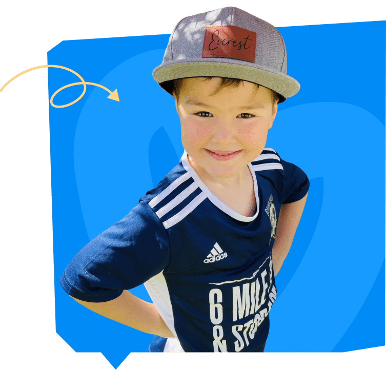 A smiling boy wearing a blue sports jersey with white stripes and a gray cap stands with his hands on his hips against a bright blue background.