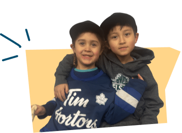 Two children smiling and posing for a photo, one wearing a Tim Hortons sweatshirt and the other in a dark hoodie.